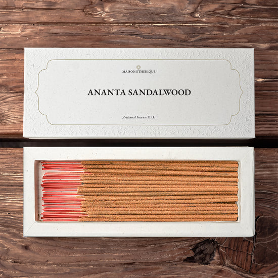 Ananta Sandalwood Incense Sticks: open white Maison Éthérique box of tan sticks with pink ends beside its lid on dark wood.