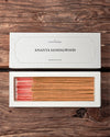 Ananta Sandalwood Incense Sticks: open white Maison Éthérique box of tan sticks with pink ends beside its lid on dark wood.