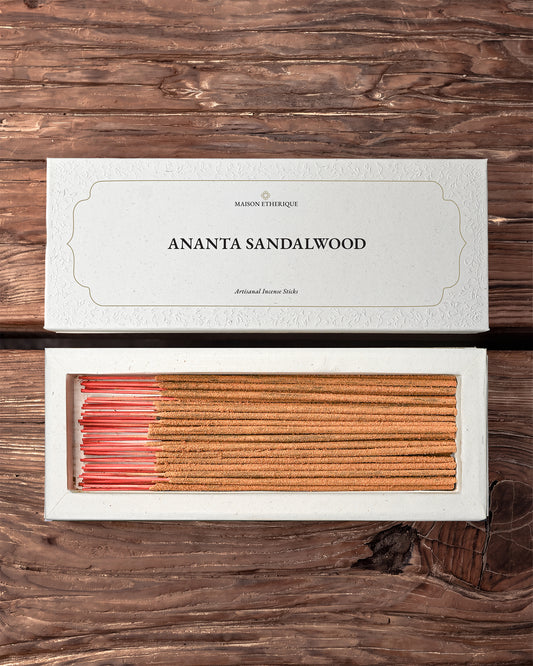 Ananta Sandalwood Incense Sticks: open white Maison Éthérique box of tan sticks with pink ends beside its lid on dark wood.
