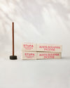 Two paper boxes of Stupa Austha Suganda incense beside a stick standing in a small holder, on a pale background.