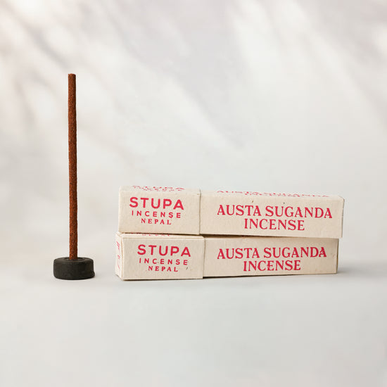 Austha Suganda incense, tube of 15 sticks: two Stupa paper boxes beside a stick standing in a small holder.