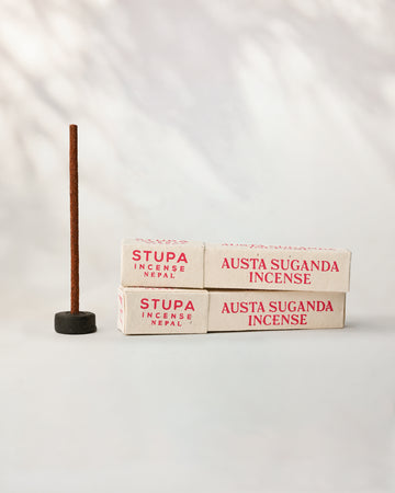 Austha Suganda incense, tube of 15 sticks: two Stupa paper boxes beside a stick standing in a small holder.