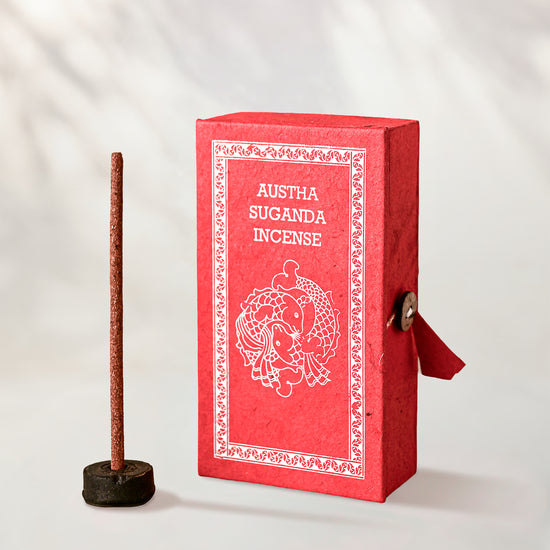 Austha Suganda Incense Sticks, box of 40: red Stupa paper box with white print beside a stick standing in a small holder.