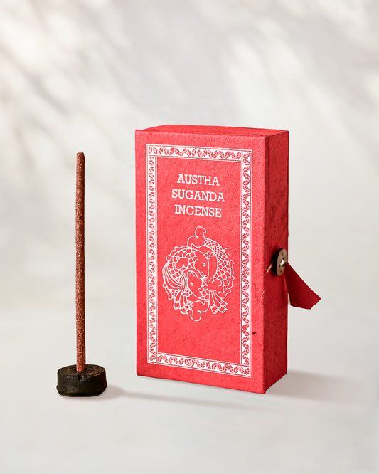 Austha Suganda Incense Sticks, box of 40: red Stupa paper box with white print beside a stick standing in a small holder.