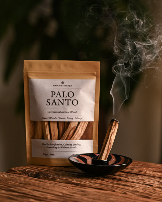 Palo Santo stick smouldering in a black ceramic burner beside a kraft pouch of Maison Éthérique Palo Santo, 100 g.