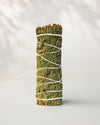Cedar smudge stick standing upright, green cedar sprigs bound with white string, on a pale surface.