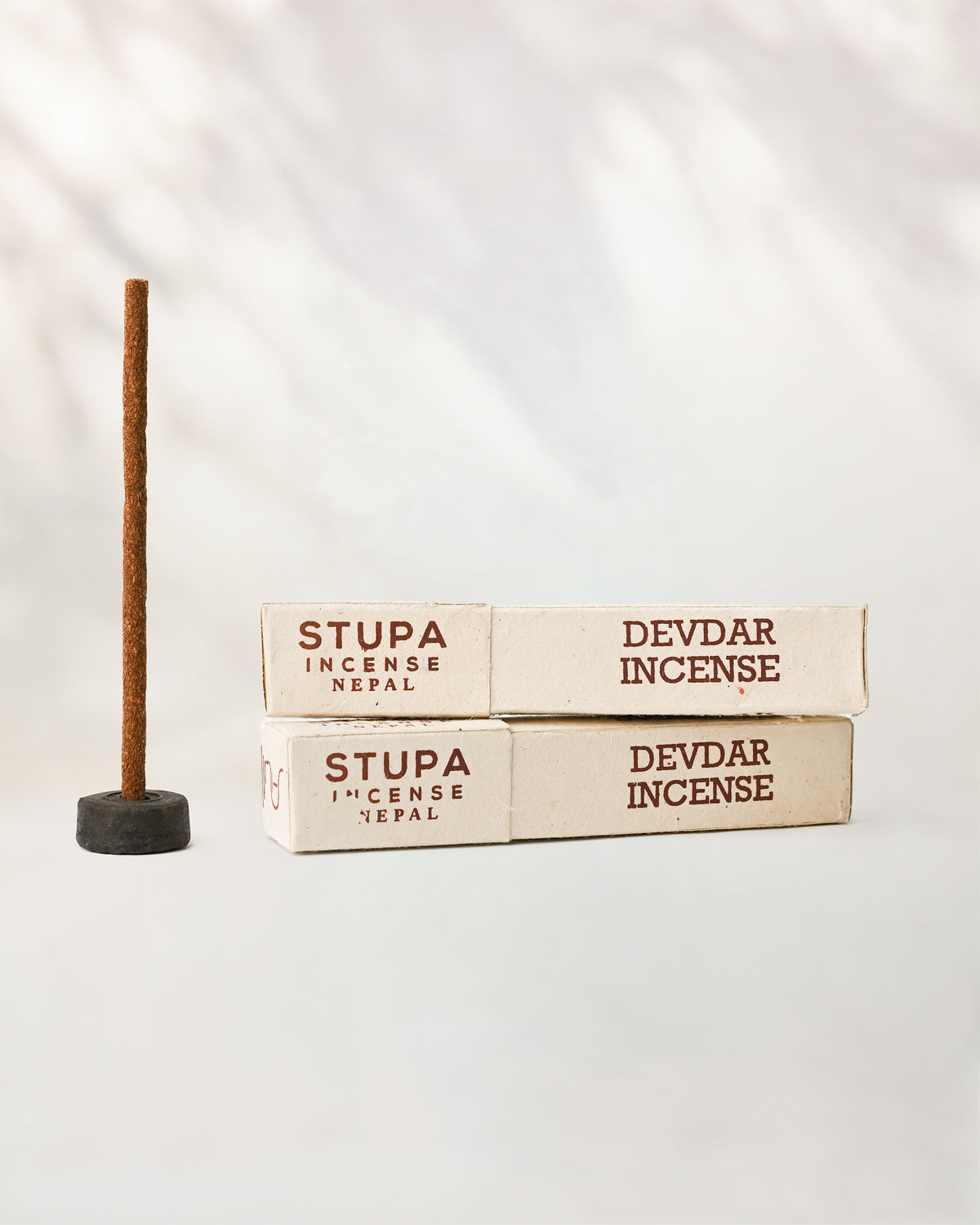 Devdar incense sticks, tube of 15: two Stupa paper boxes beside a stick standing in a small holder.