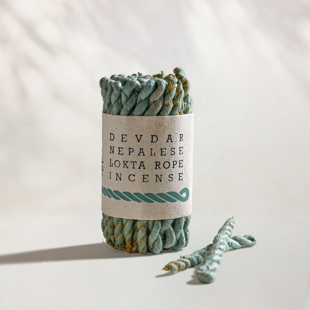 Devdar Lokta Rope Incense Bundle: green twisted rope incense in a kraft paper band, two loose ropes beside it.