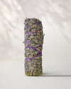 Lavender smudge stick (Lavandula angustifolia) standing upright, flower heads bound with purple string, on a pale surface.
