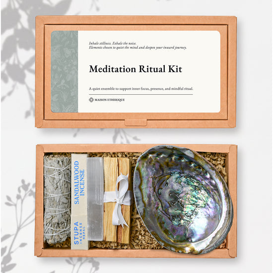 Meditation Ritual Kit: kraft box lid above the open box with a white sage stick, sandalwood incense, Palo Santo and an abalone shell.