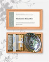 Meditation Ritual Kit: kraft box lid above the open box with a white sage stick, sandalwood incense, Palo Santo and an abalone shell.