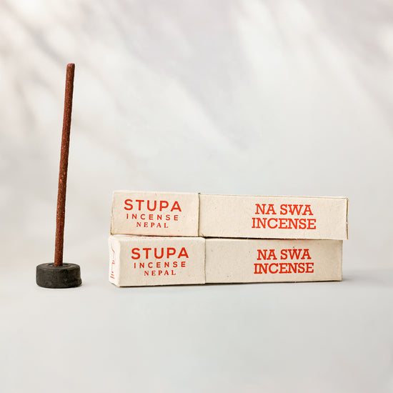 Na Swa incense, tube of 15 sticks: two Stupa paper boxes beside a stick standing in a small holder.