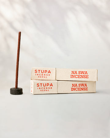 Na Swa incense, tube of 15 sticks: two Stupa paper boxes beside a stick standing in a small holder.
