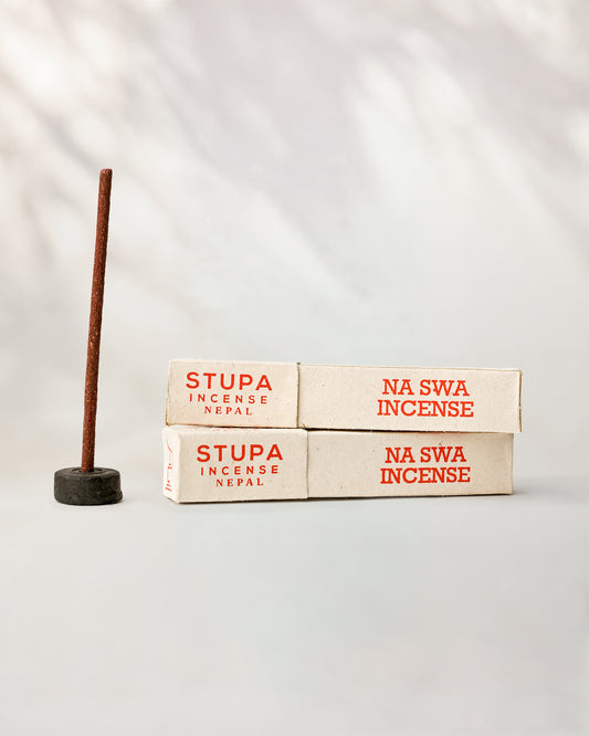 Na Swa incense, tube of 15 sticks: two Stupa paper boxes beside a stick standing in a small holder.