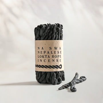 Na Swa Lokta Rope Incense Bundle: charcoal twisted rope incense in a kraft paper band, two loose ropes beside it.