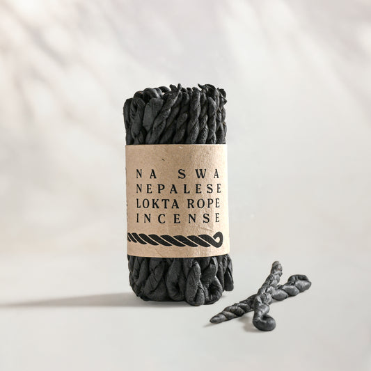 Na Swa Lokta Rope Incense Bundle: charcoal twisted rope incense in a kraft paper band, two loose ropes beside it.
