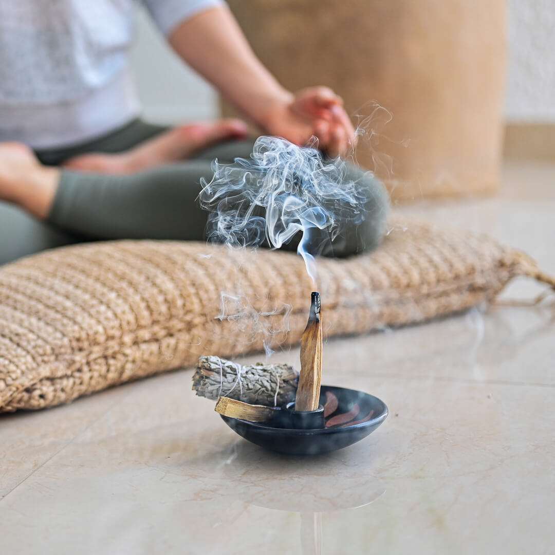 A woman meditating with burning Palo Santo