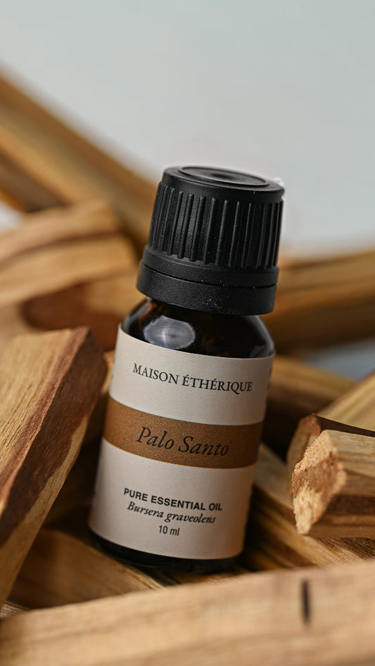 10 ml bottle of Maison Éthérique Palo Santo essential oil resting on Palo Santo sticks.