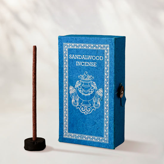 Sandalwood Stupa Incense Sticks, box of 40: blue paper box with white print beside a stick standing in a small holder.