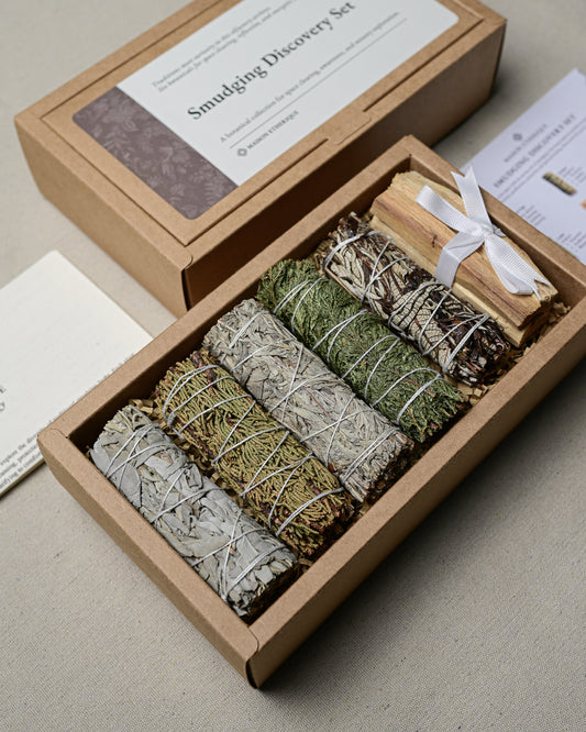 Open Smudging Discovery Set seen at an angle, five smudge sticks and ribbon-tied Palo Santo in a kraft box.