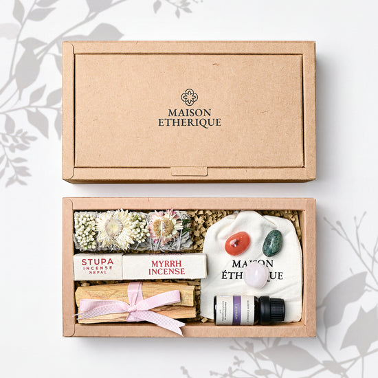 Whispers of Joy: open kraft Maison Éthérique box holding a herb bundle, myrrh incense, Palo Santo, lavender oil and tumbled stones.