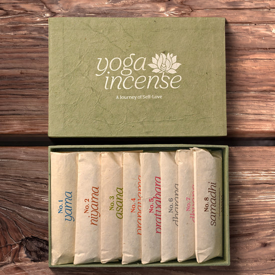 Yoga Incense Gift Box: green handmade paper box with its lid off, eight numbered paper packets of incense inside, on dark wood.