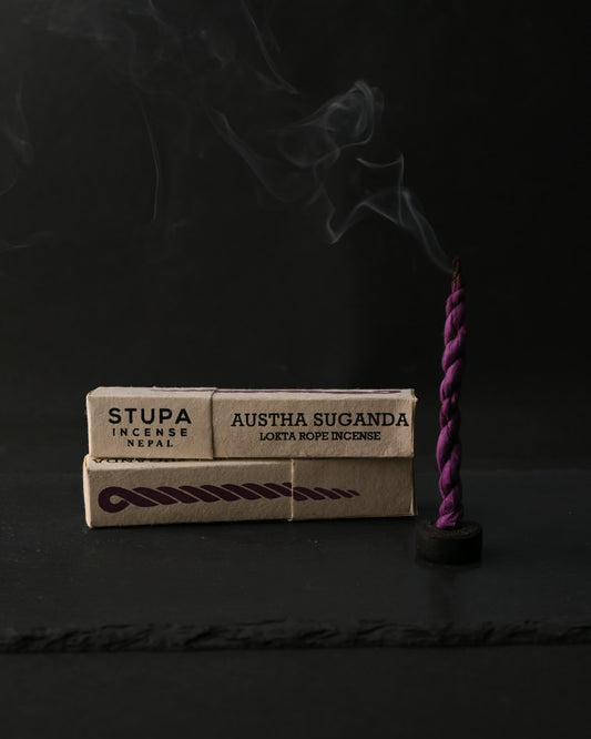Two boxes of Stupa Austha Suganda lokta rope incense beside a purple rope incense burning upright on a dark background.
