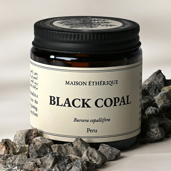 Amber glass jar of Maison Éthérique Black Copal from Peru with grey-black copal pieces arranged around its base.