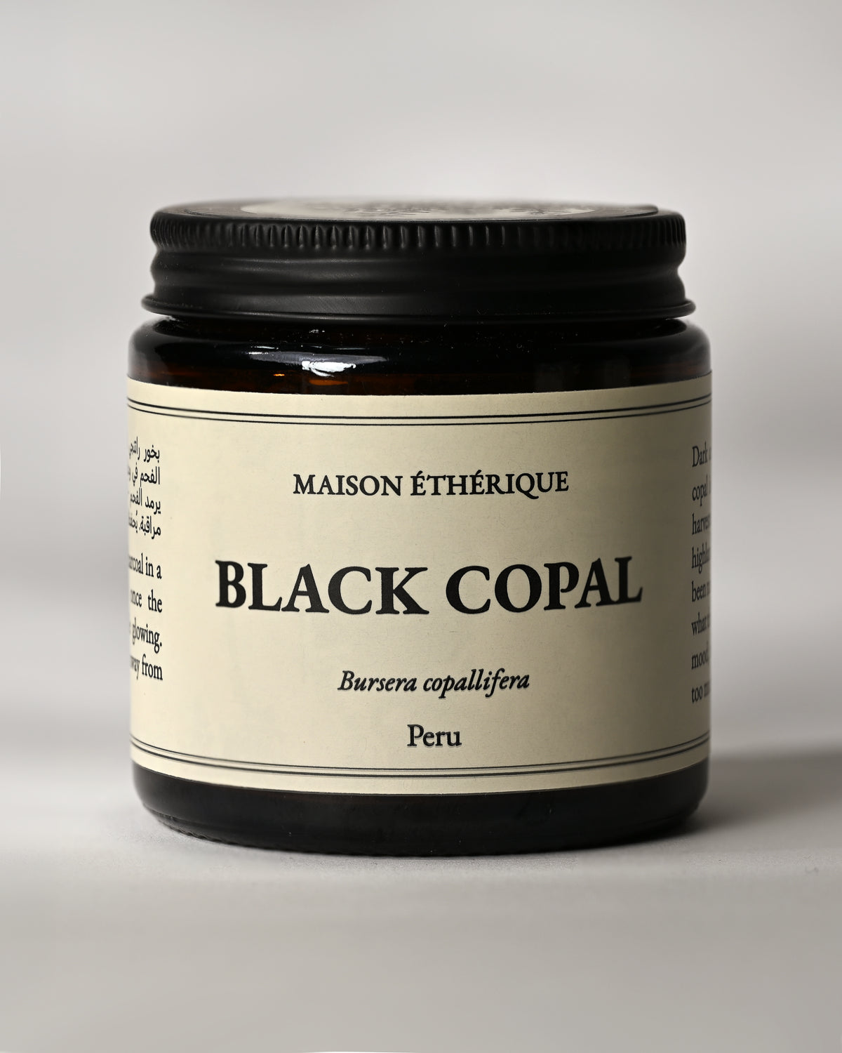 Amber glass jar of Maison Éthérique Black Copal from Peru, black lid, on a pale background.