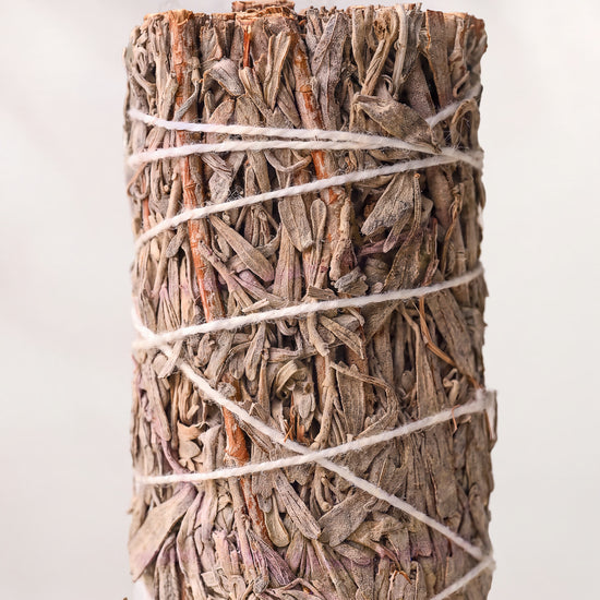 Blue sage smudge stick, dried blue sage leaves bound with white string, shown close against a pale background.