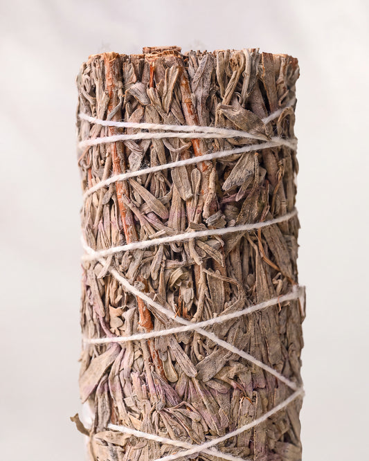 Blue sage smudge stick, dried blue sage leaves bound with white string, shown close against a pale background.