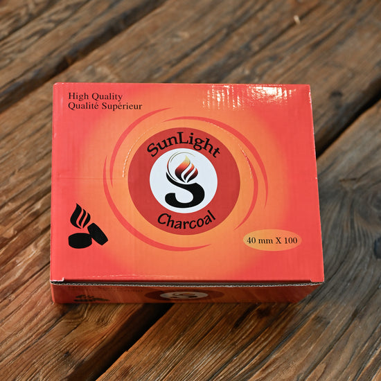 Closed orange box of charcoal tablets for resin burning, on a wooden surface.