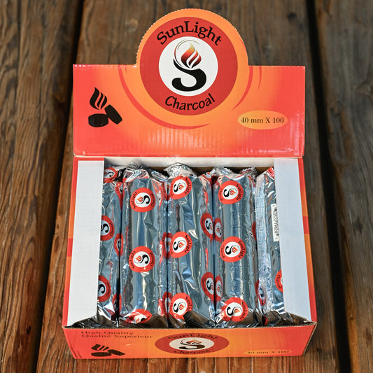 Open box of charcoal tablets for resin burning, foil-wrapped rolls visible, on a wooden surface.