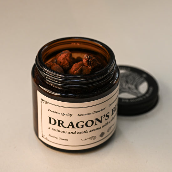 Open amber jar of Maison Éthérique Dragon's Blood resin with its lid beside it, on a pale background.
