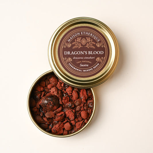 Open gold tin of Maison Éthérique Dragon's Blood resin (Dracaena cinnabari), the lid resting on the tin and red resin pieces visible.