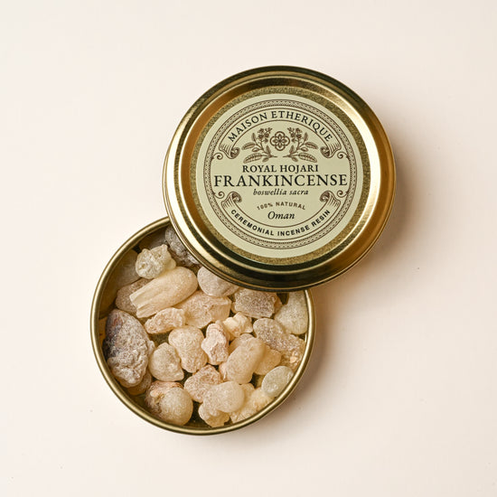 Open gold tin of Maison Éthérique Hojari frankincense (Boswellia sacra) from Oman, pale resin tears visible inside.