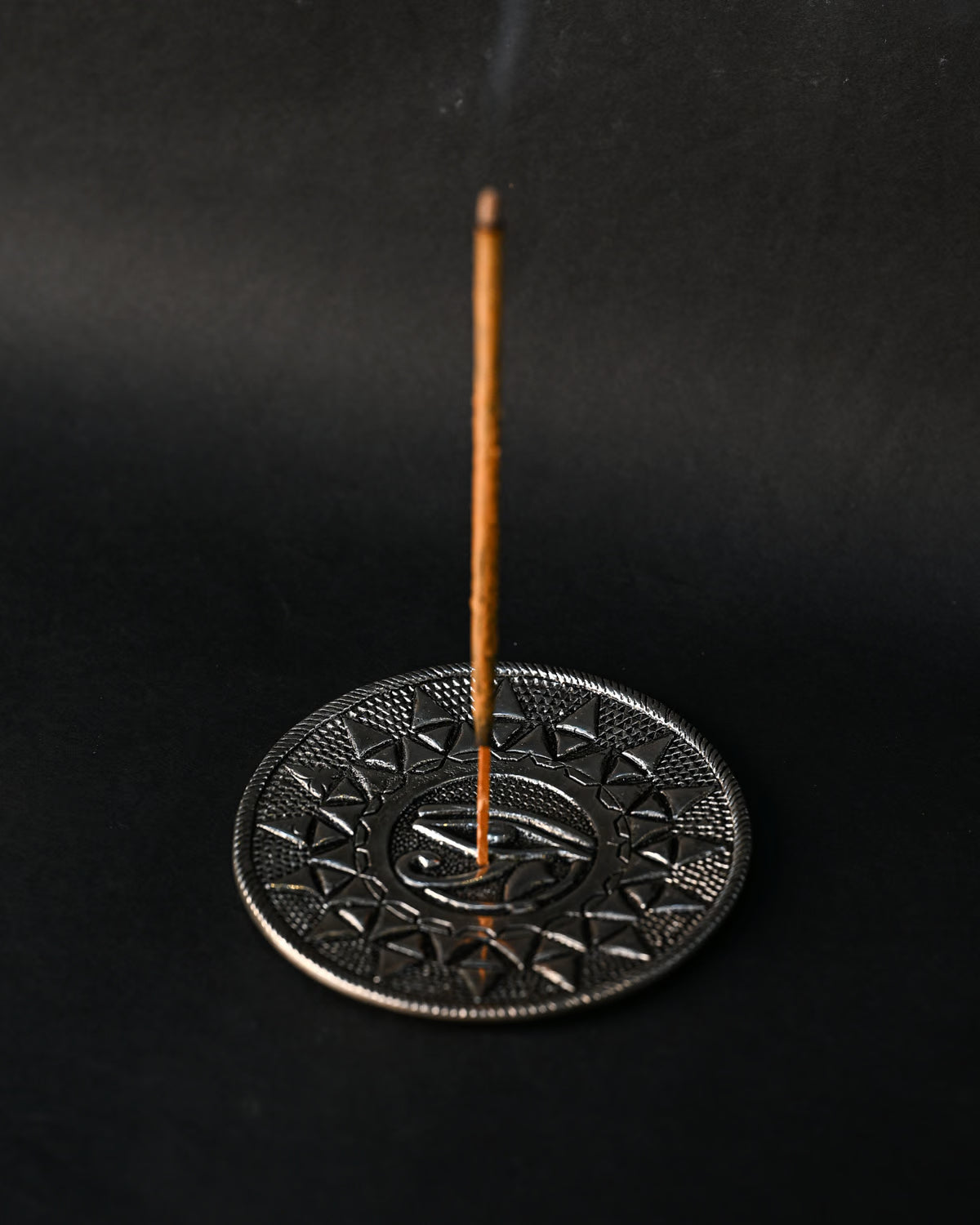 Incense stick standing upright in the Eye of Horus metal holder against a dark background.