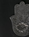 Close view of the hand-shaped metal incense holder, showing the embossed eye and floral detail.