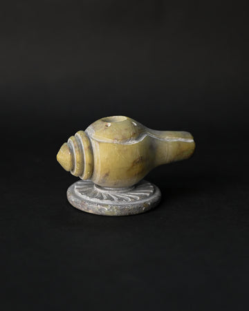 Shankh incense stick holder carved from green-yellow stone in the form of a conch, on a dark background.