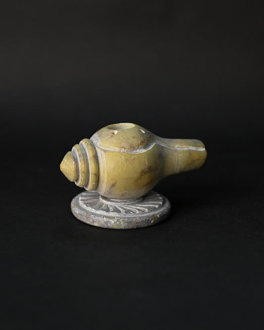 Shankh incense stick holder carved from green-yellow stone in the form of a conch, on a dark background.