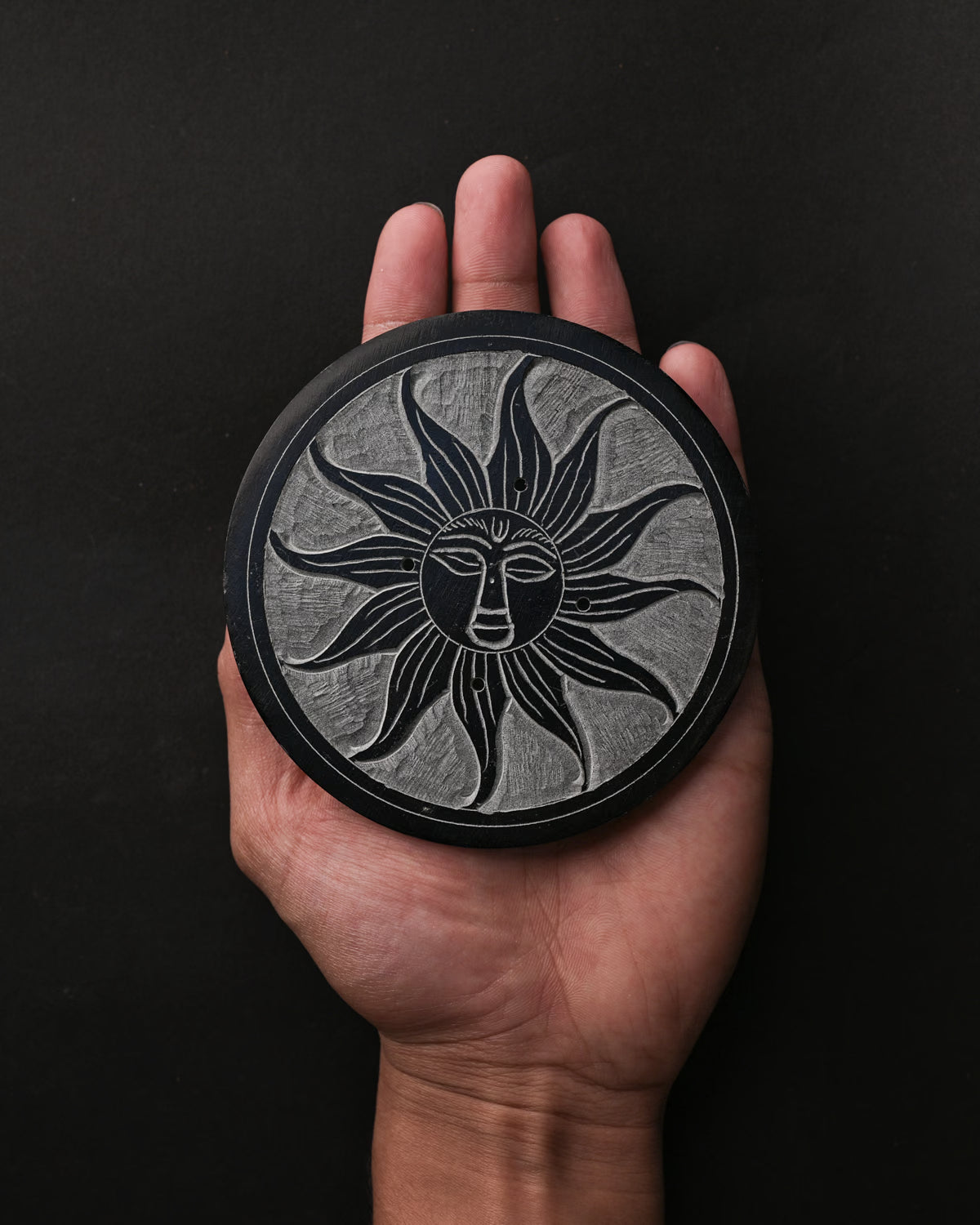 Soleil Noir carved stone incense holder resting on an open palm.