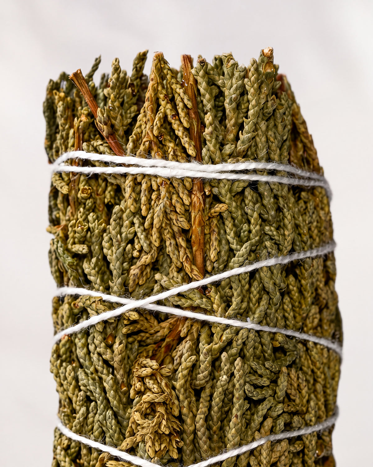 Juniper smudge stick, dried green juniper sprigs bound with white string, shown close against a pale background.