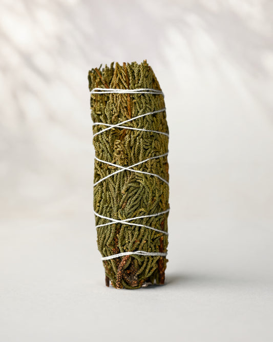 Juniper smudge stick standing upright, green juniper sprigs bound with white string, on a pale surface.
