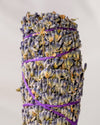 Lavender smudge stick, dried lavender flower heads bound with purple string, shown close against a pale background.