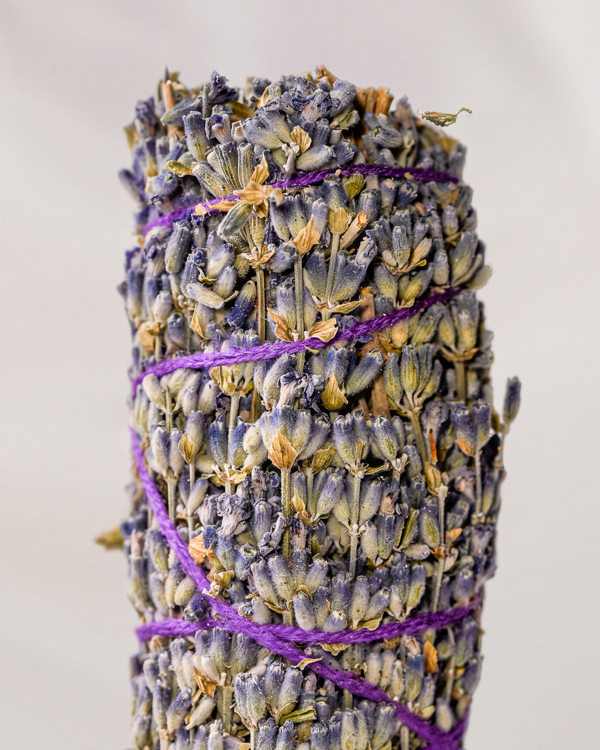 Lavender smudge stick, dried lavender flower heads bound with purple string, shown close against a pale background.