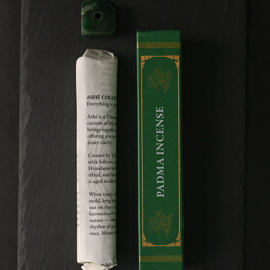 Padma Tibetan incense: paper-wrapped bundle, green box and small green holder laid out on dark slate.
