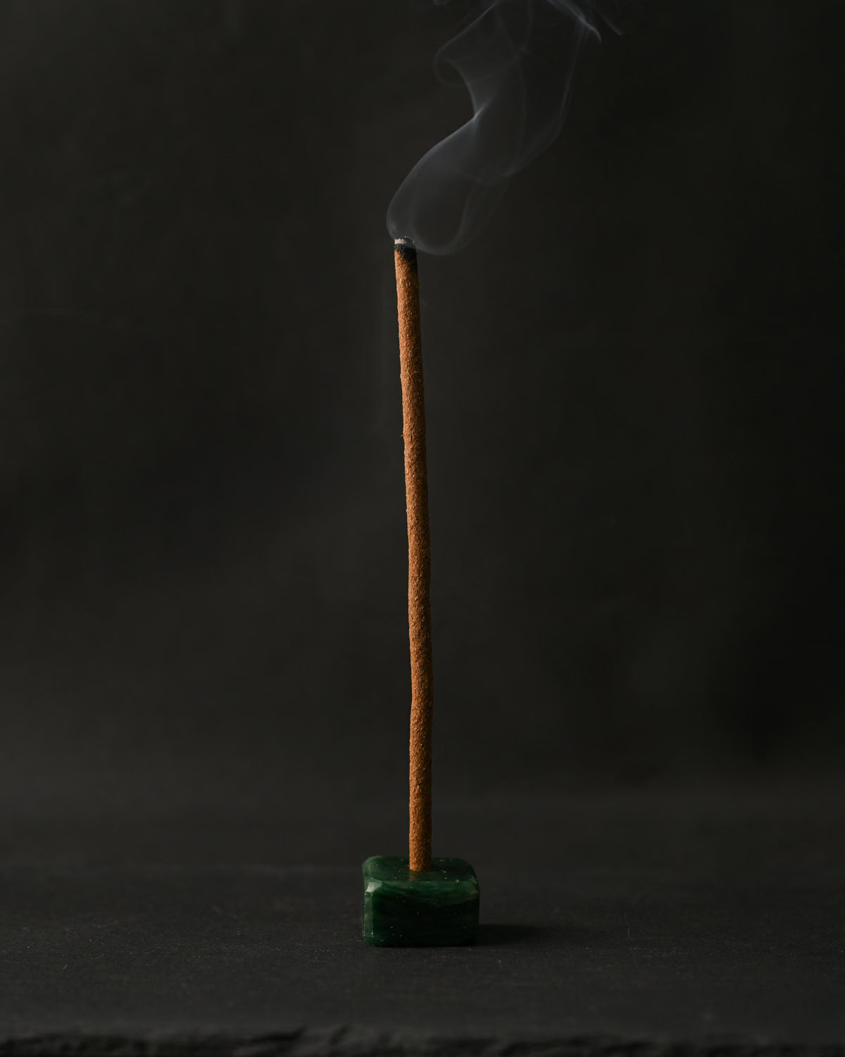 Padma Tibetan incense stick burning upright in a small green holder, smoke curling against a dark background.