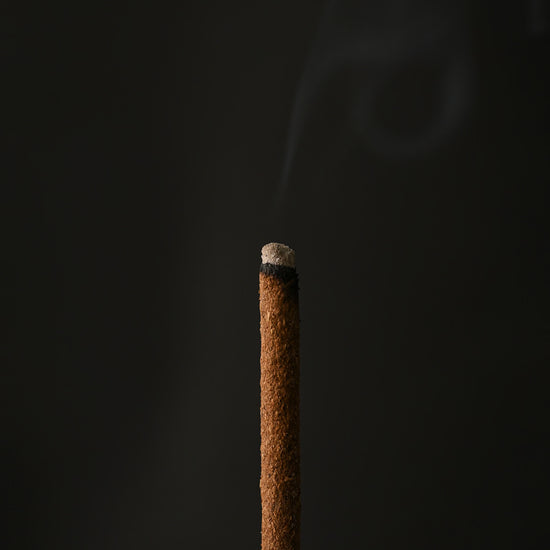 Close view of the glowing tip of a Padma Tibetan incense stick with a wisp of smoke.