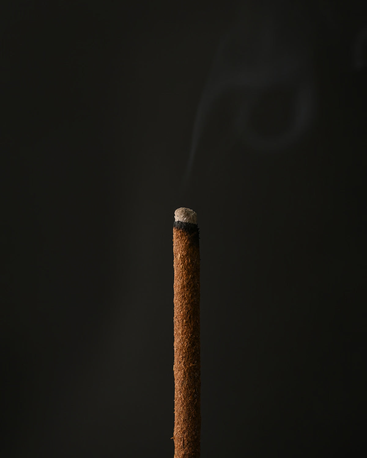 Close view of the glowing tip of a Padma Tibetan incense stick with a wisp of smoke.
