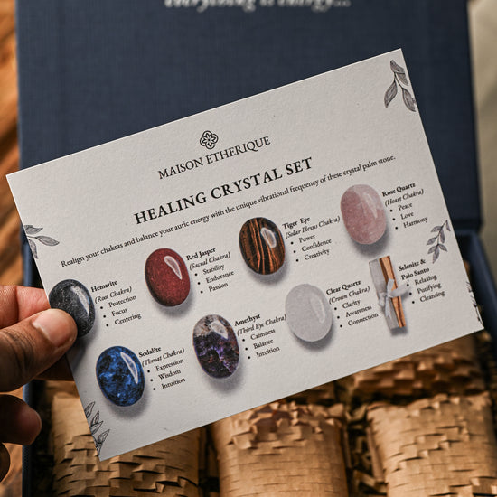 Hand holding the printed guide card of the Maison Éthérique palm stones crystal set above its paper-lined box.